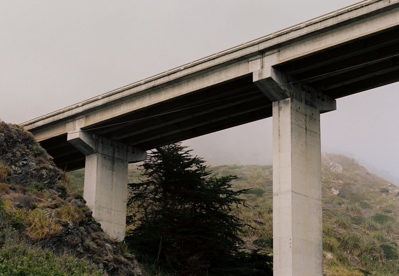 An image shot from below of a tall bridge with a gray sky above it